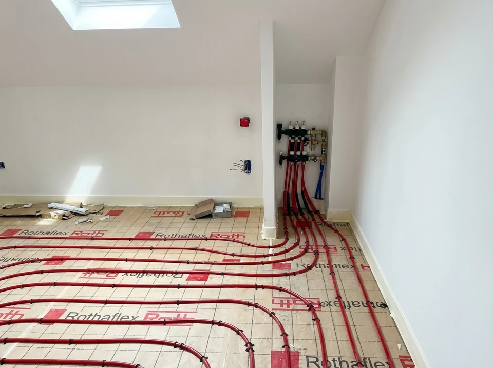 Un plombier en vêtement de travail bleu installe ou répare un sèche-serviettes chromé dans une salle de bains carrelée blanc