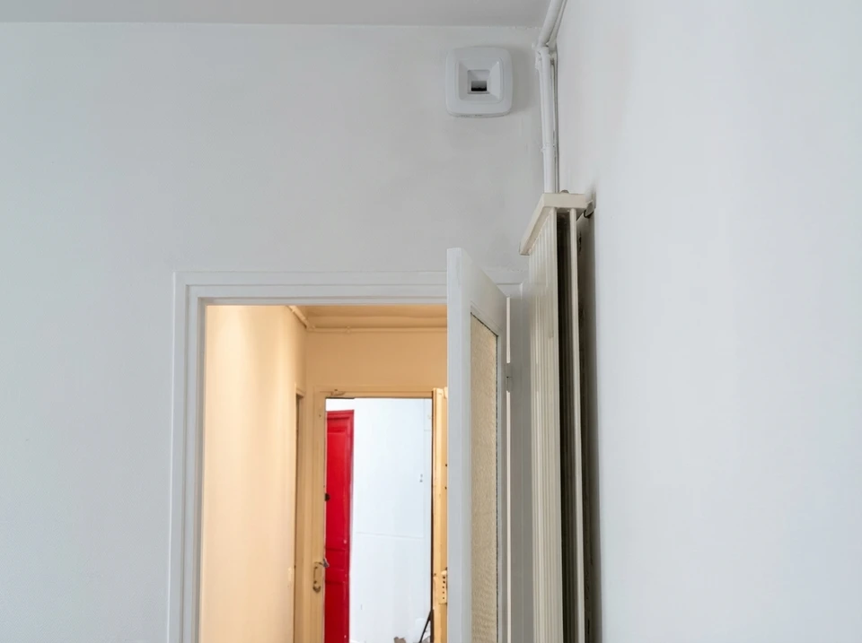 Installateur en gants de protection blancs et bleus positionnant une grille d'aération ventilation dans plafond blanc d'intérieur résidentiel