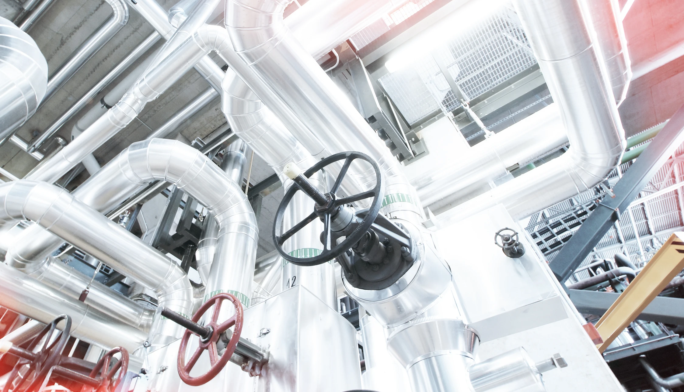 Installation industrielle avec réseau complexe de tuyauteries métalliques isolées thermiquement, vannes de régulation à volant manuel rouge et noir, raccords coudés, système de chauffage ou refroidissement