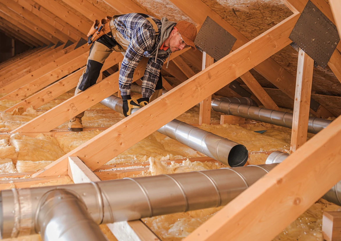 Ouvrier en combinaison à carreaux travaille dans les combles d'une habitation, installant ou réparant un système de ventilation